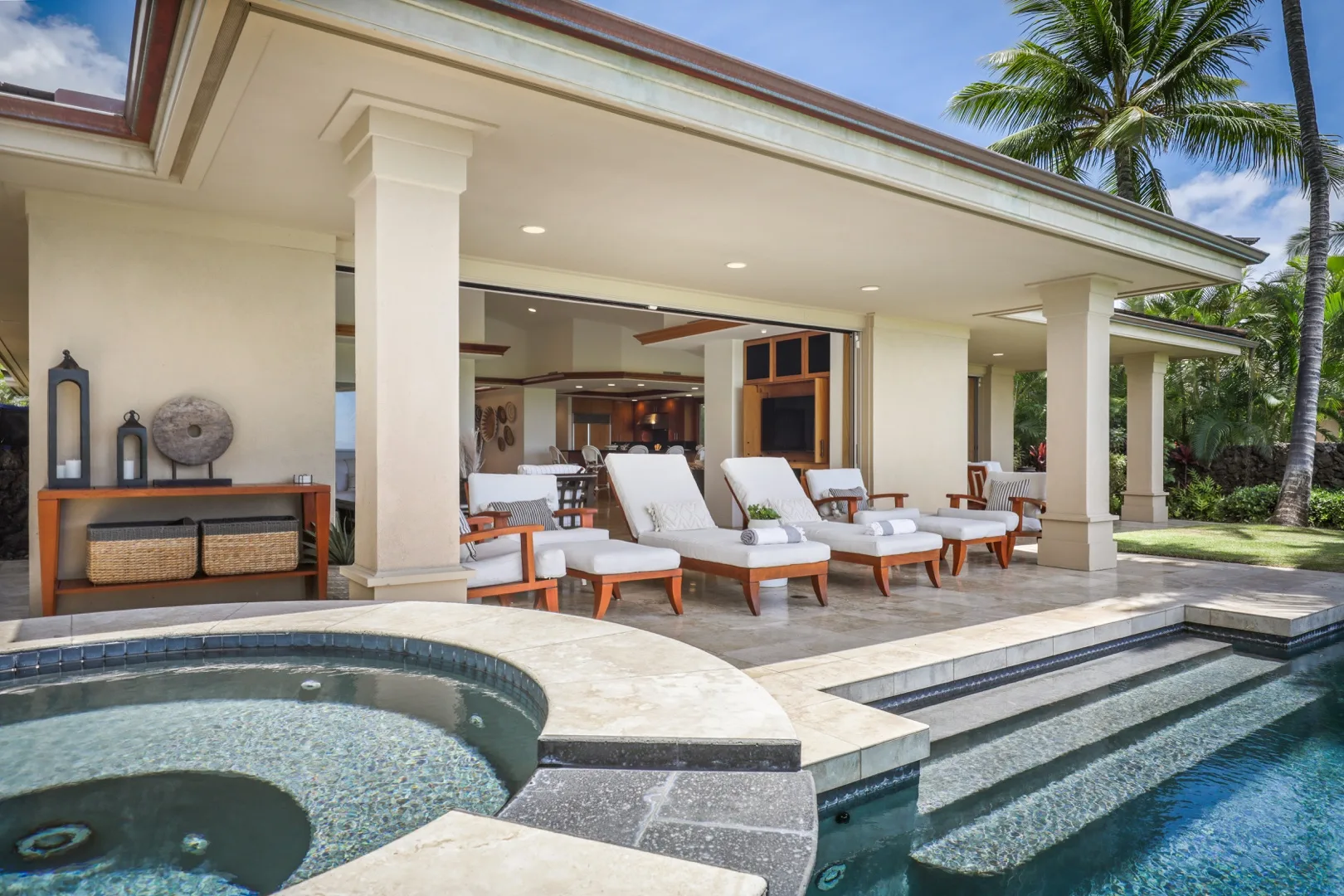 An open-air patio with lounge seating beside a swimming pool and spa.