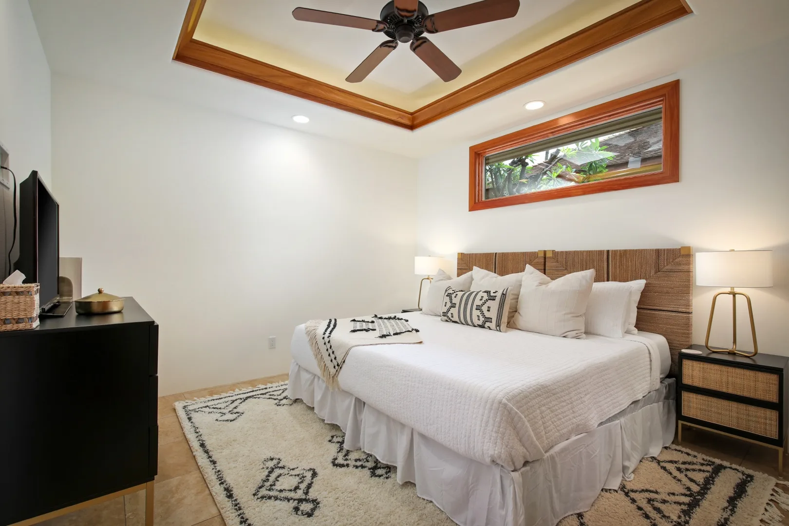A bedroom with a neatly made bed, patterned rug, and ceiling fan.