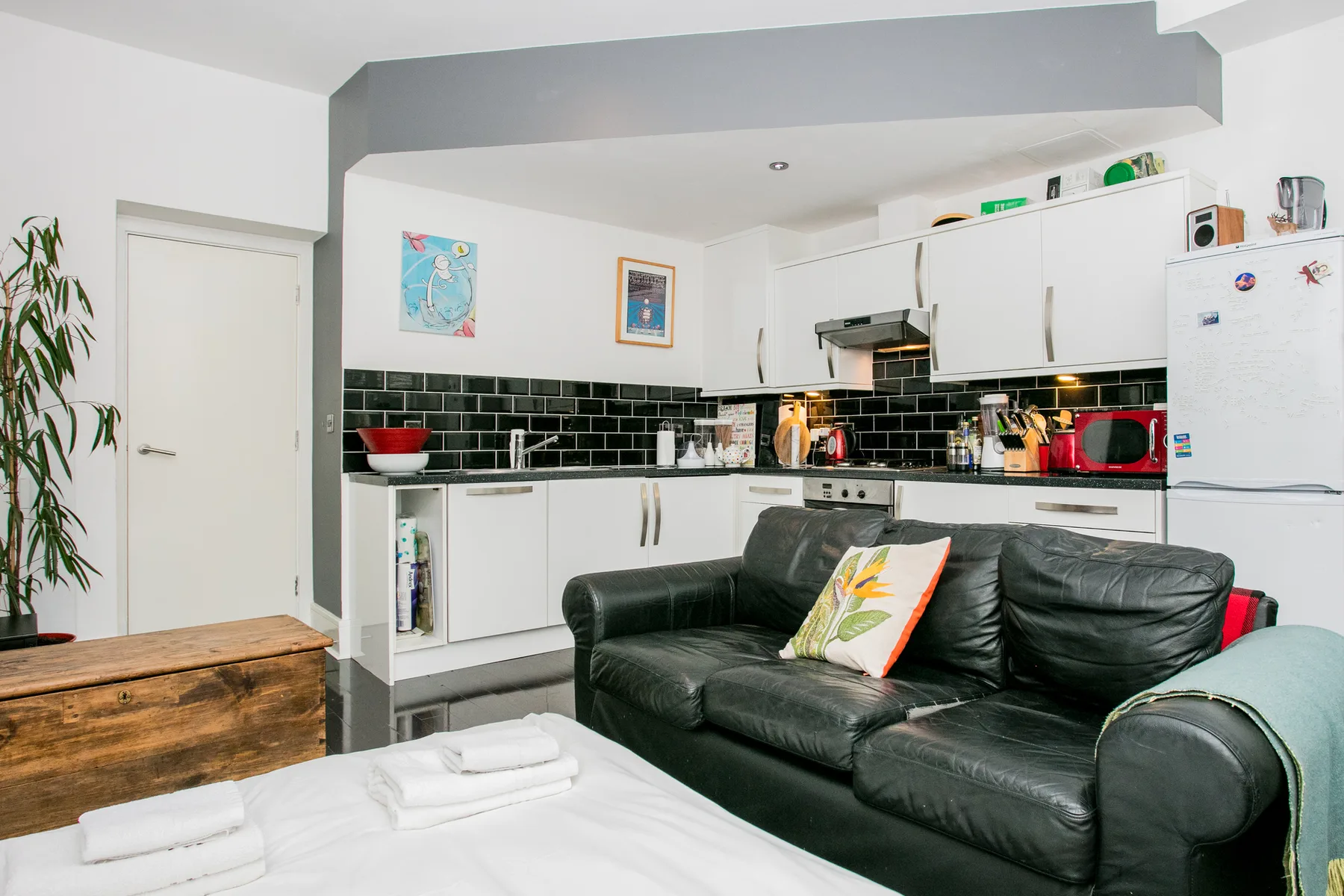 A living area with a black sofa in front of a compact kitchen.