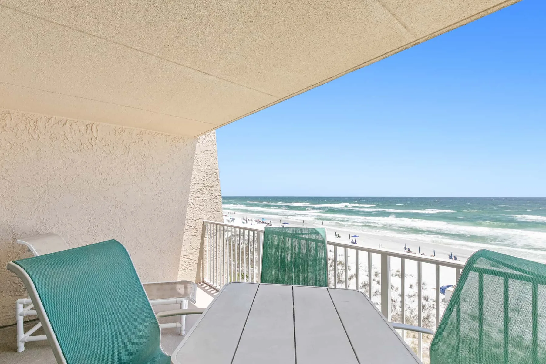 A covered seaside balcony has a table and seating overlooking the ocean.