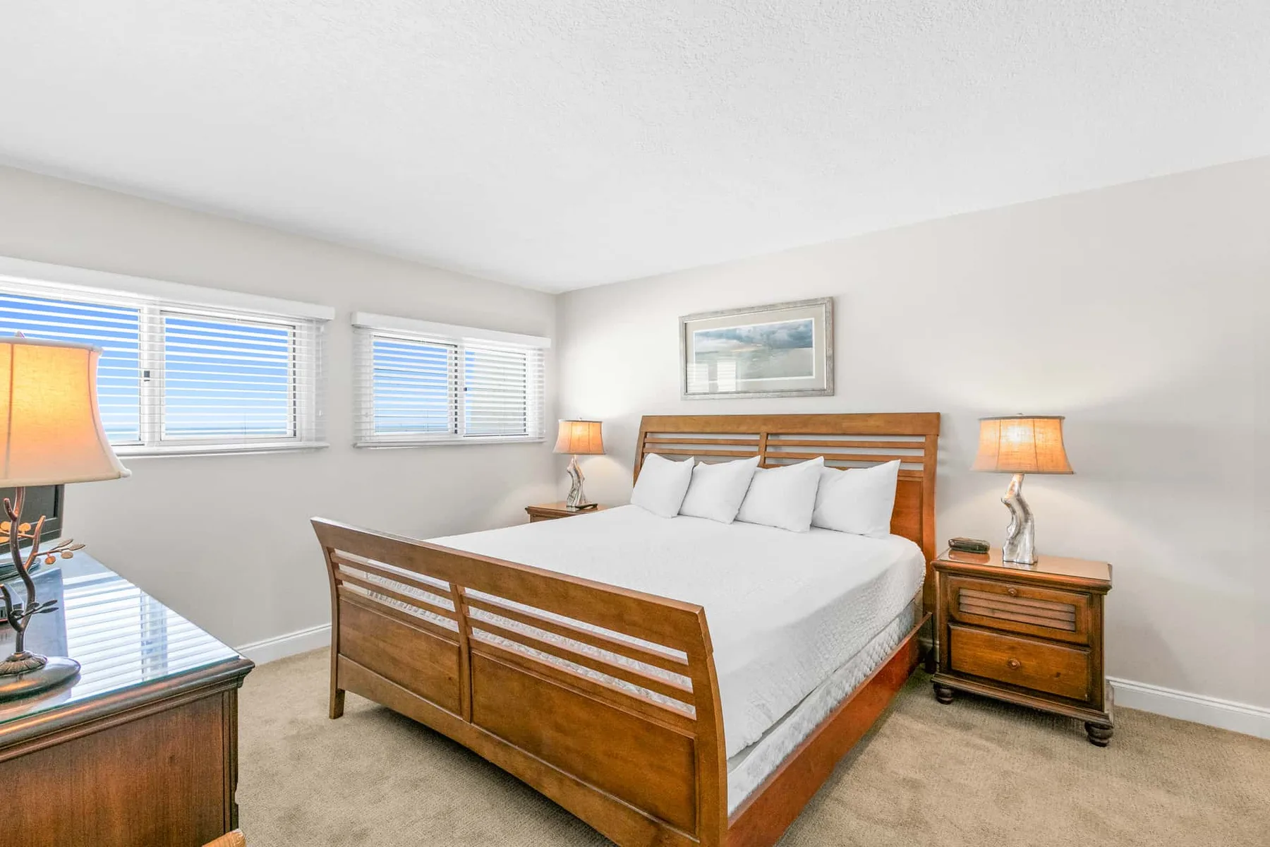 A bedroom with a wooden bed, white bedding, and windows with blinds.