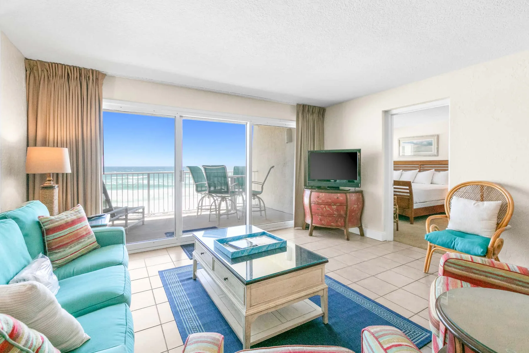 A bright living room opens onto a balcony, with seating and a television.