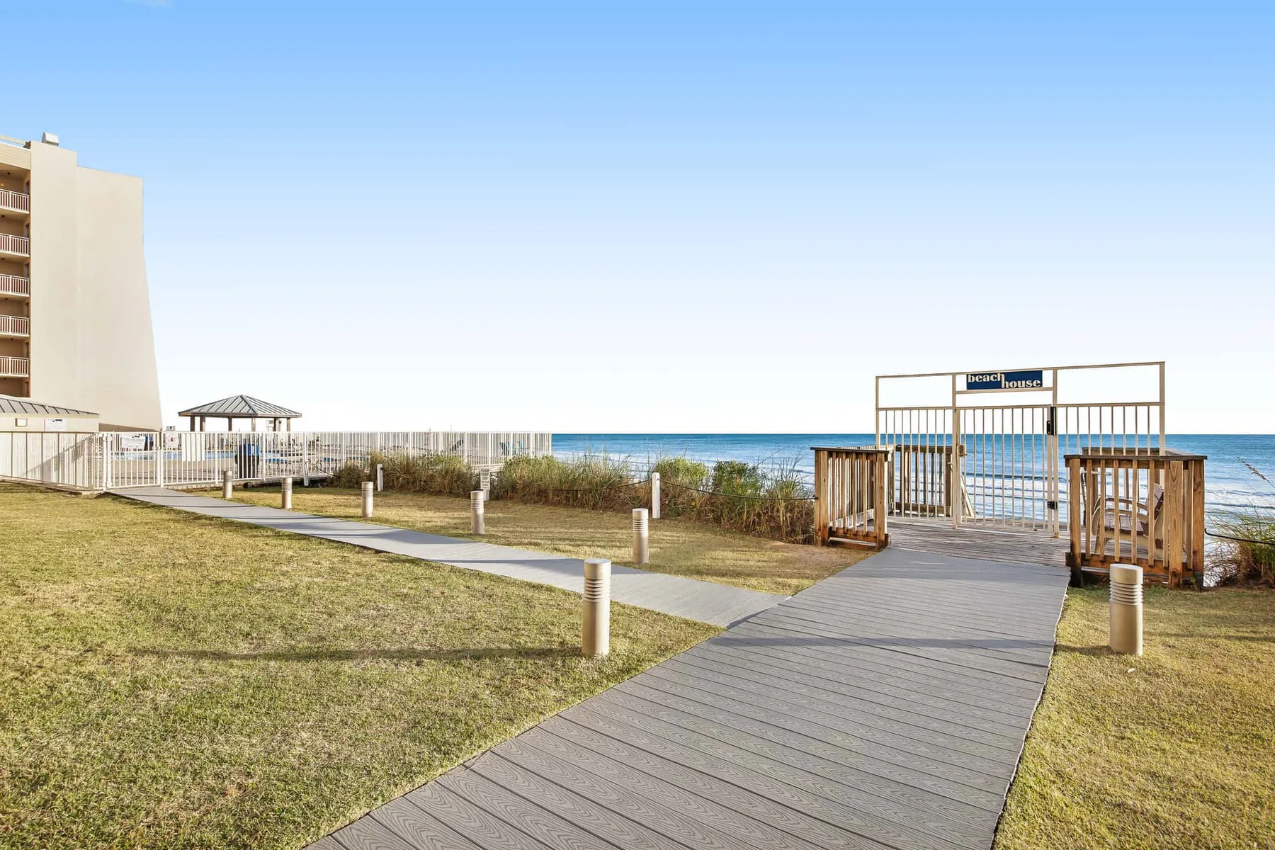 A boardwalk crosses a grassy beachfront toward an entrance by the ocean.