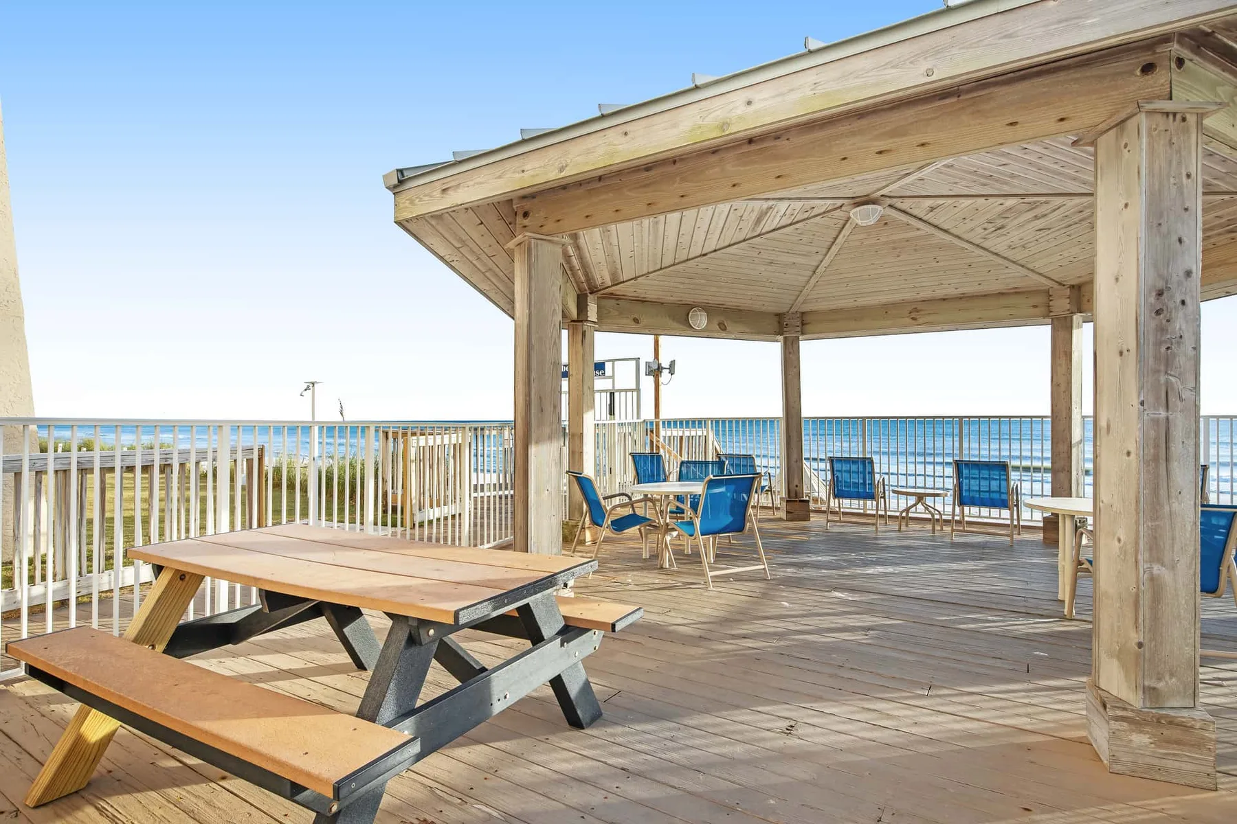 A wooden seaside deck with a covered seating area and picnic table overlooks the water.