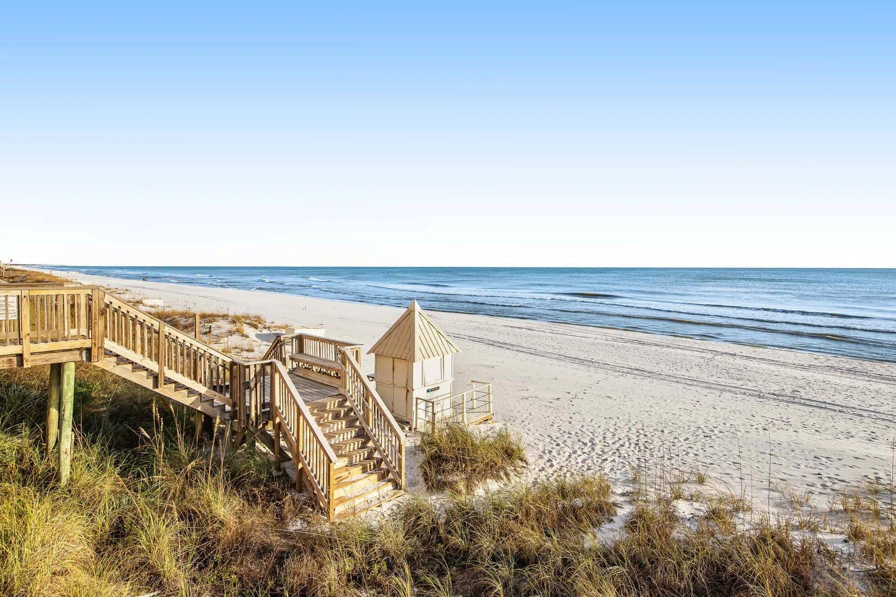A beach access walkway crosses grassy dunes beside the ocean.