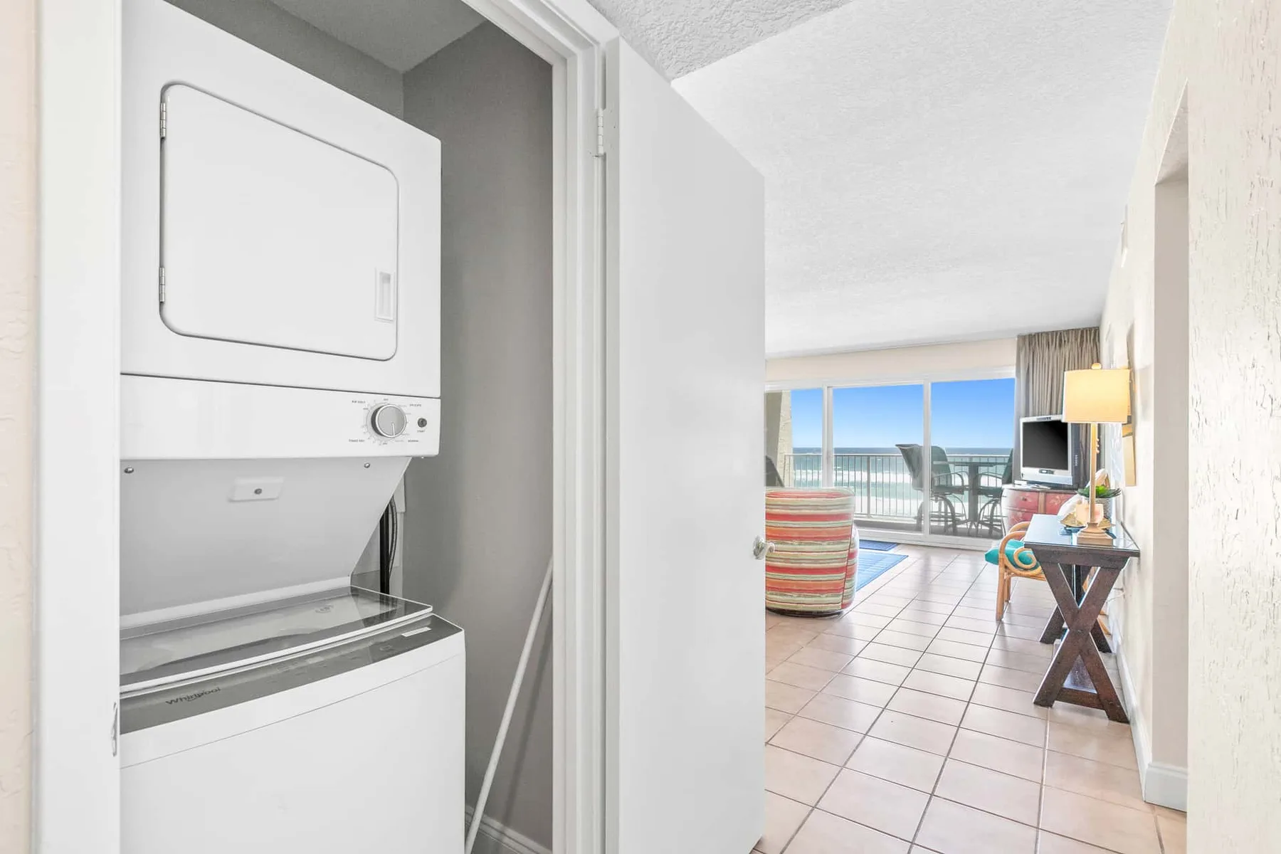 A laundry area opens onto a living space with seating and large windows.