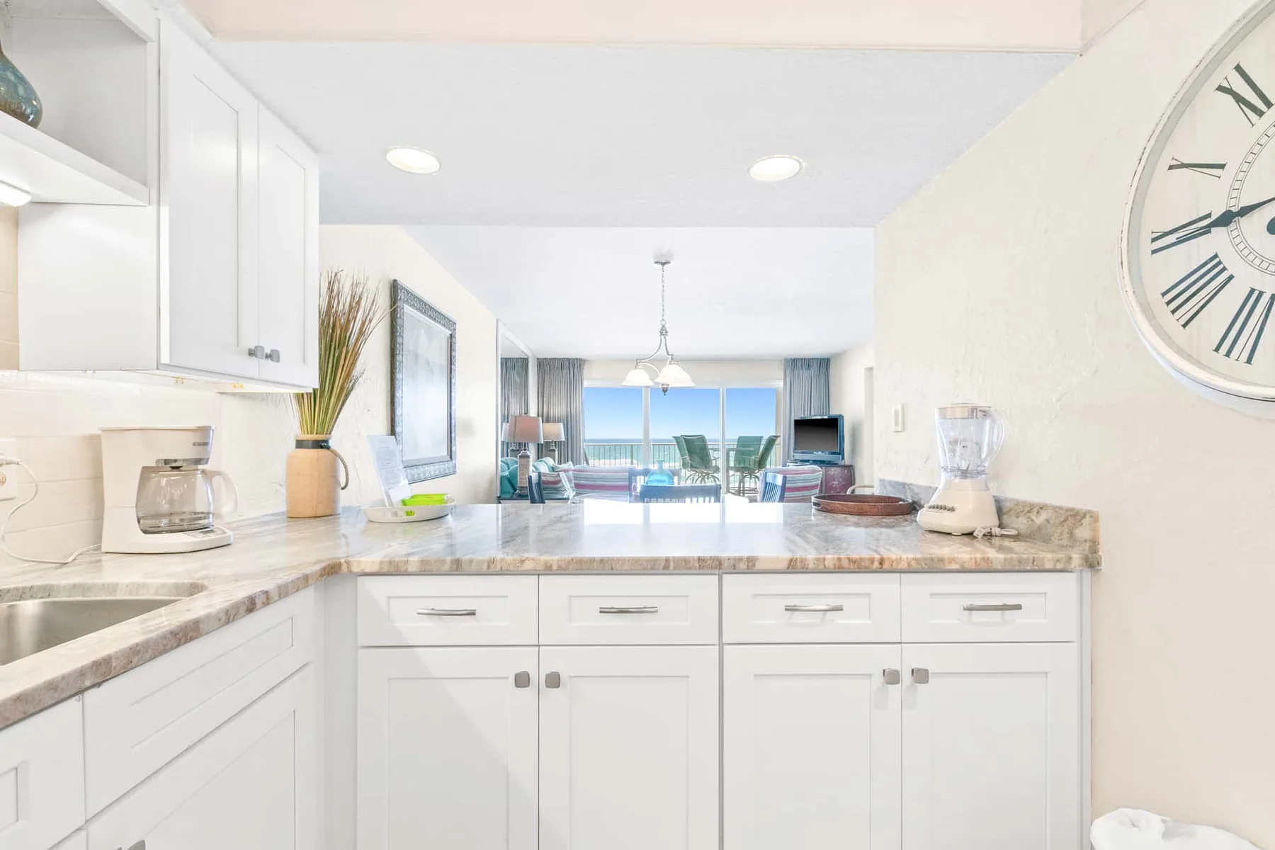 A bright kitchen with white cabinets and a counter overlooking a living area.