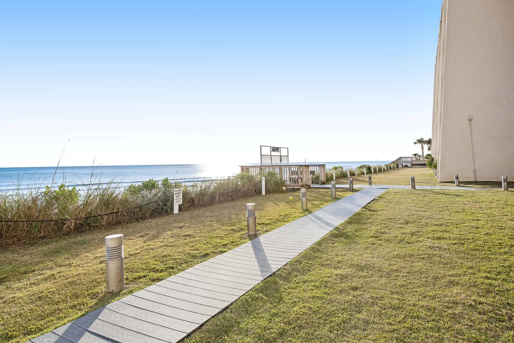 A seaside walkway crosses grassy grounds beside the beach.