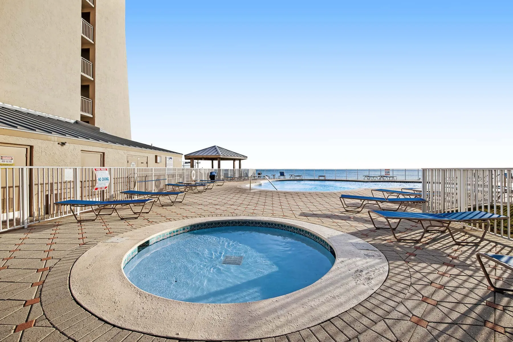 An outdoor pool sits on a paved deck beside the ocean.