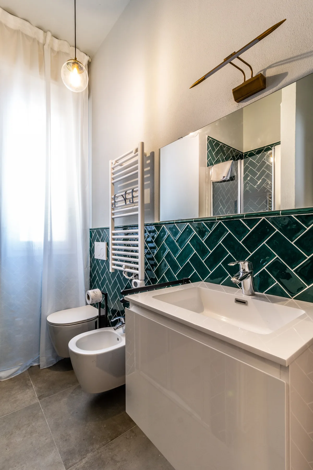 Un baño moderno con lavabo, inodoro y paredes de azulejos verde oscuro.