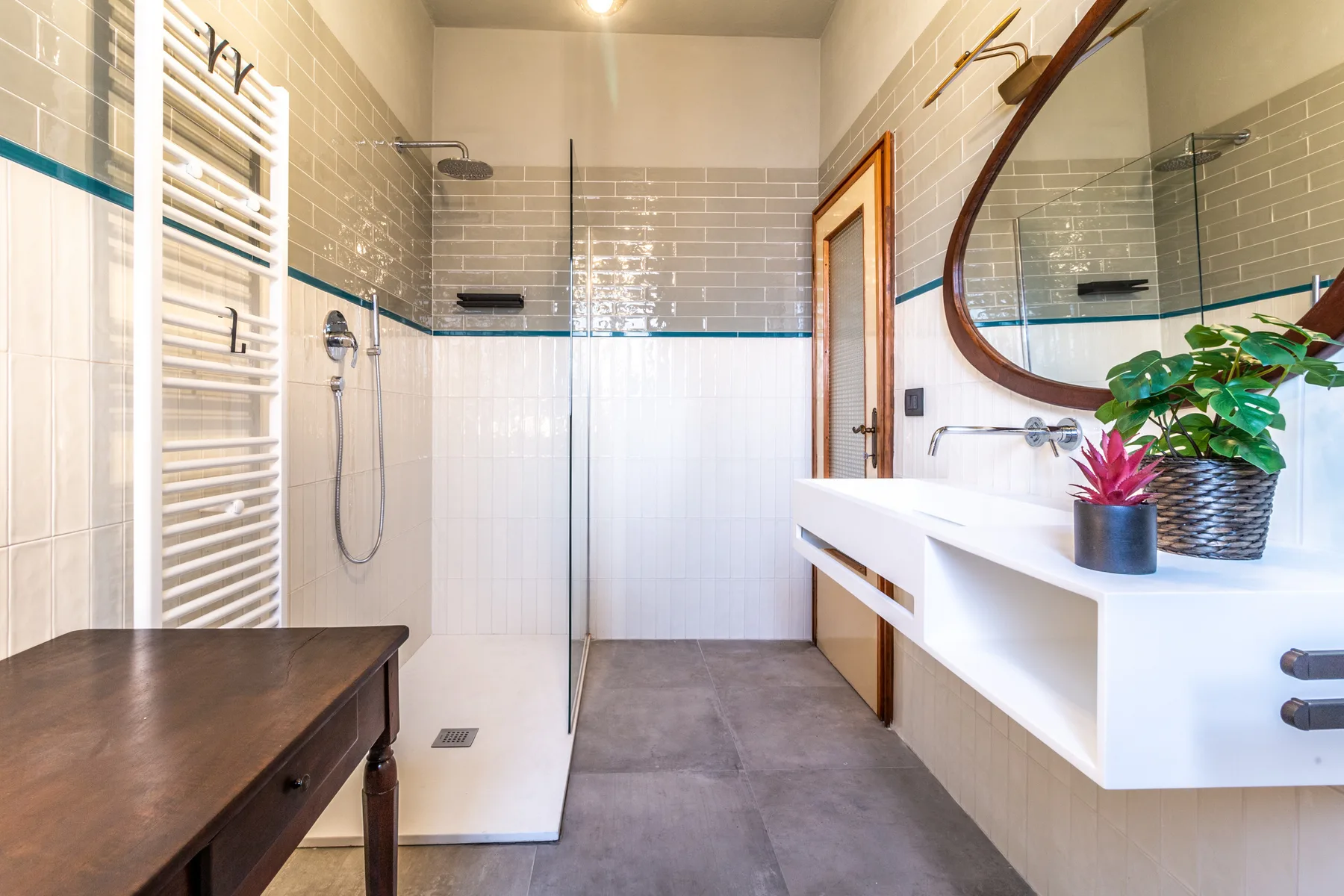 Un baño luminoso con ducha de cristal, lavabo suspendido y espejo redondo.