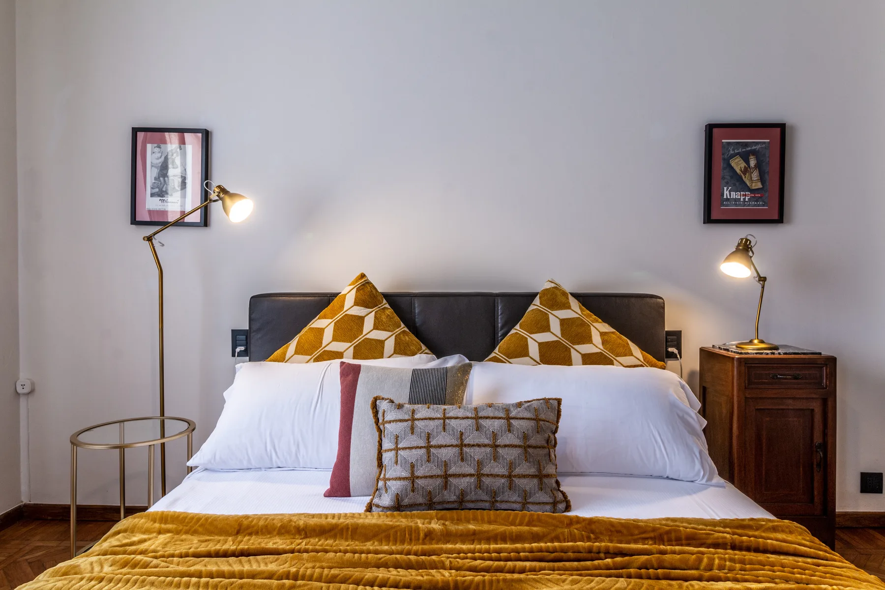 Un dormitorio con una cama bien arreglada, cojines estampados y lámparas de noche.