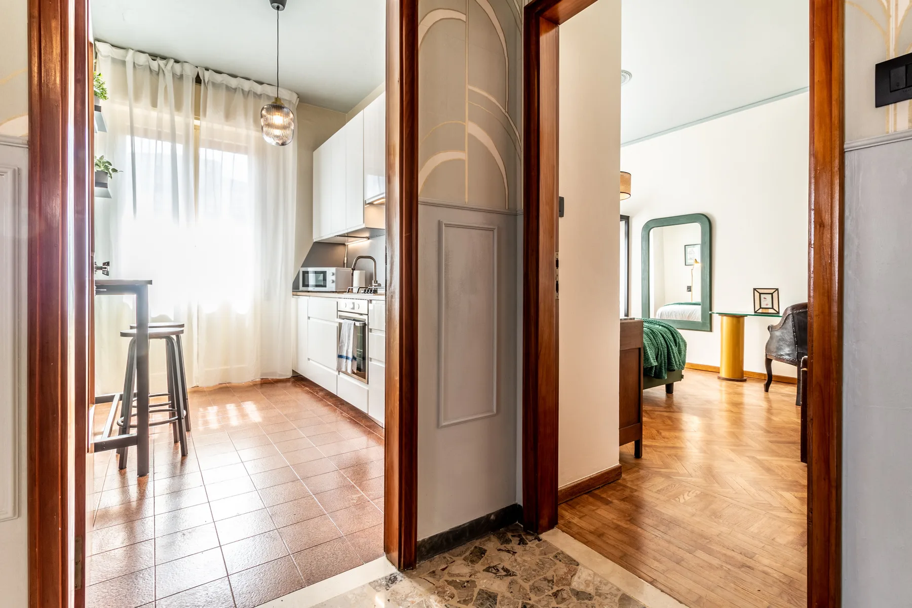 Una cocina luminosa con armarios blancos y una barra de comedor se abre a un dormitorio.