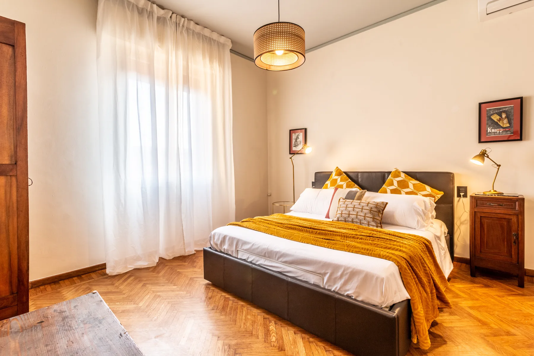 A bedroom with a bed dressed in white linens and a mustard-colored throw.