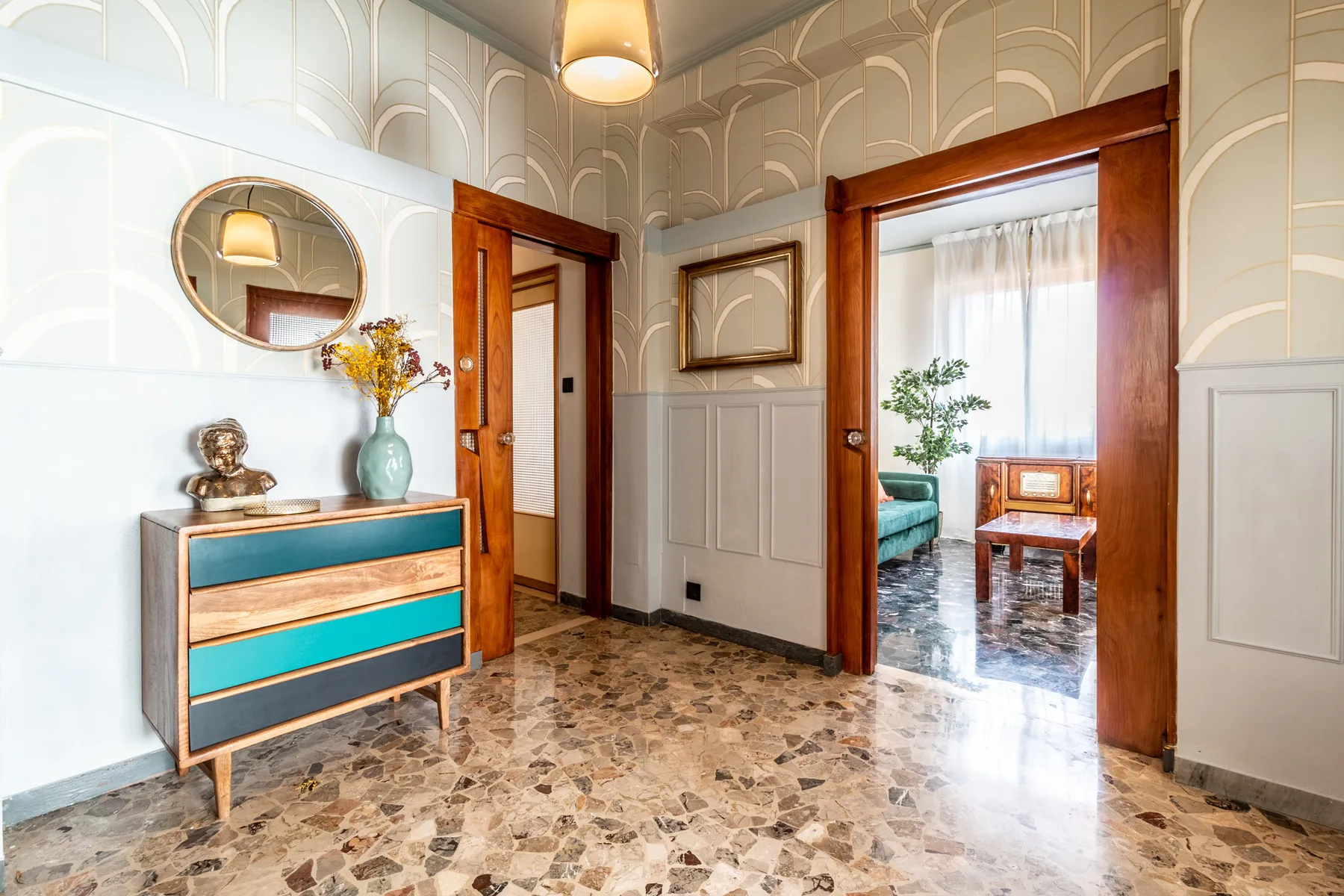 Un pasillo interior luminoso da a una sala de estar, con suelo de baldosas estampadas.