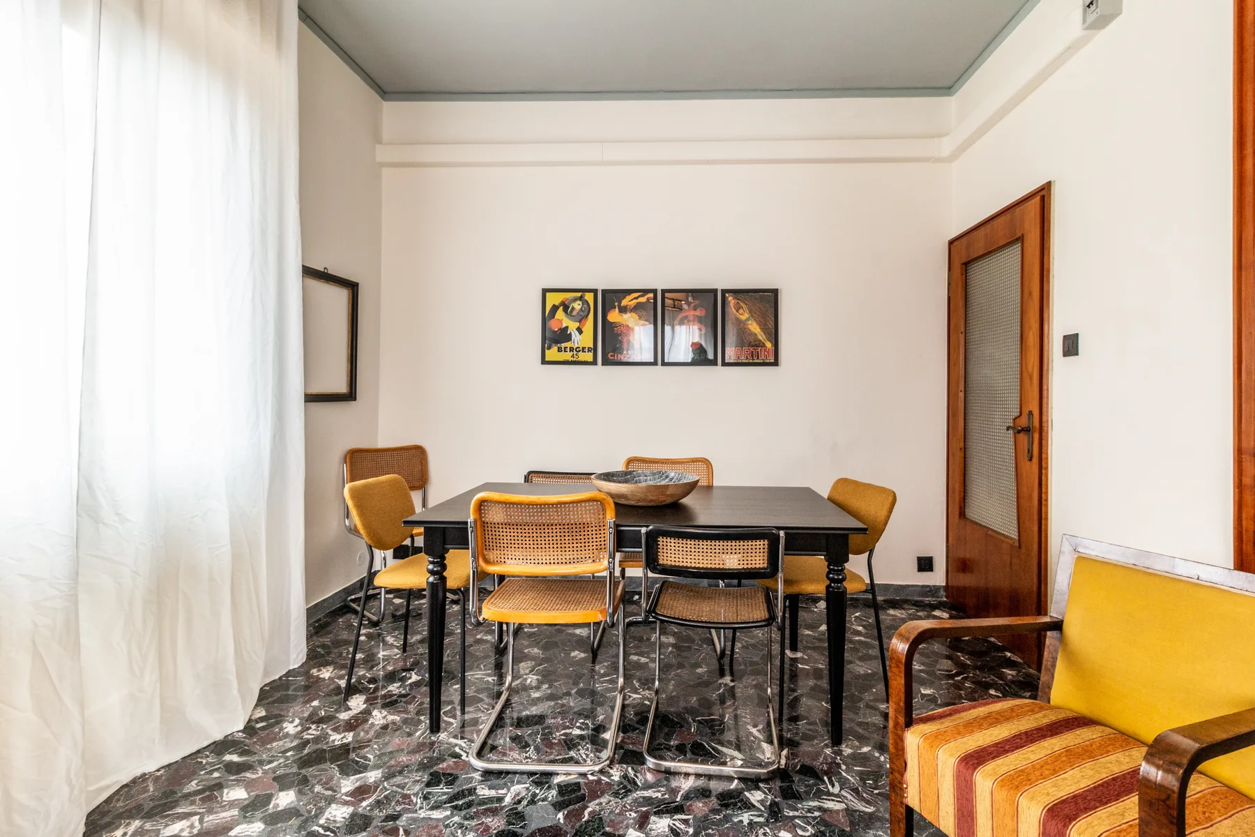 Un comedor con una mesa oscura y asientos junto a una ventana con cortinas.
