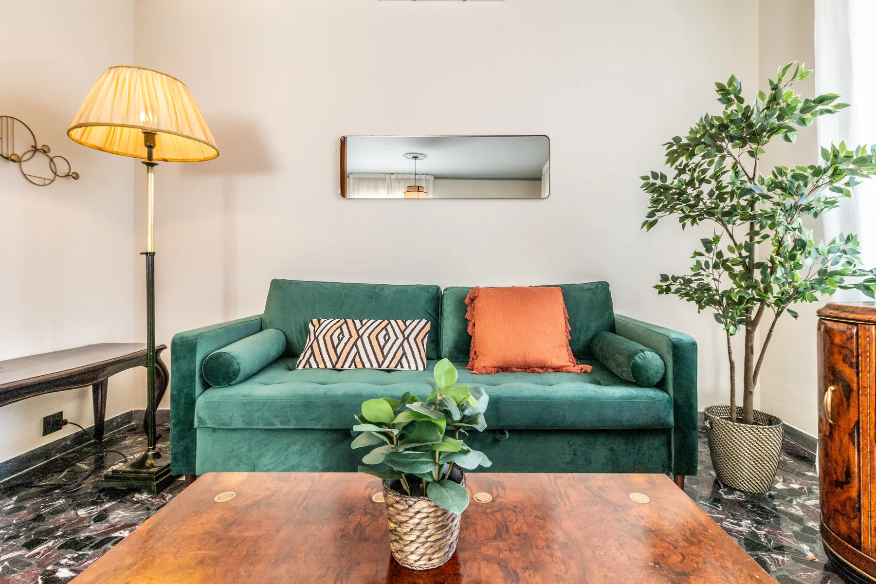 Una sala de estar con asientos verdes, una lámpara de pie y una planta frondosa.