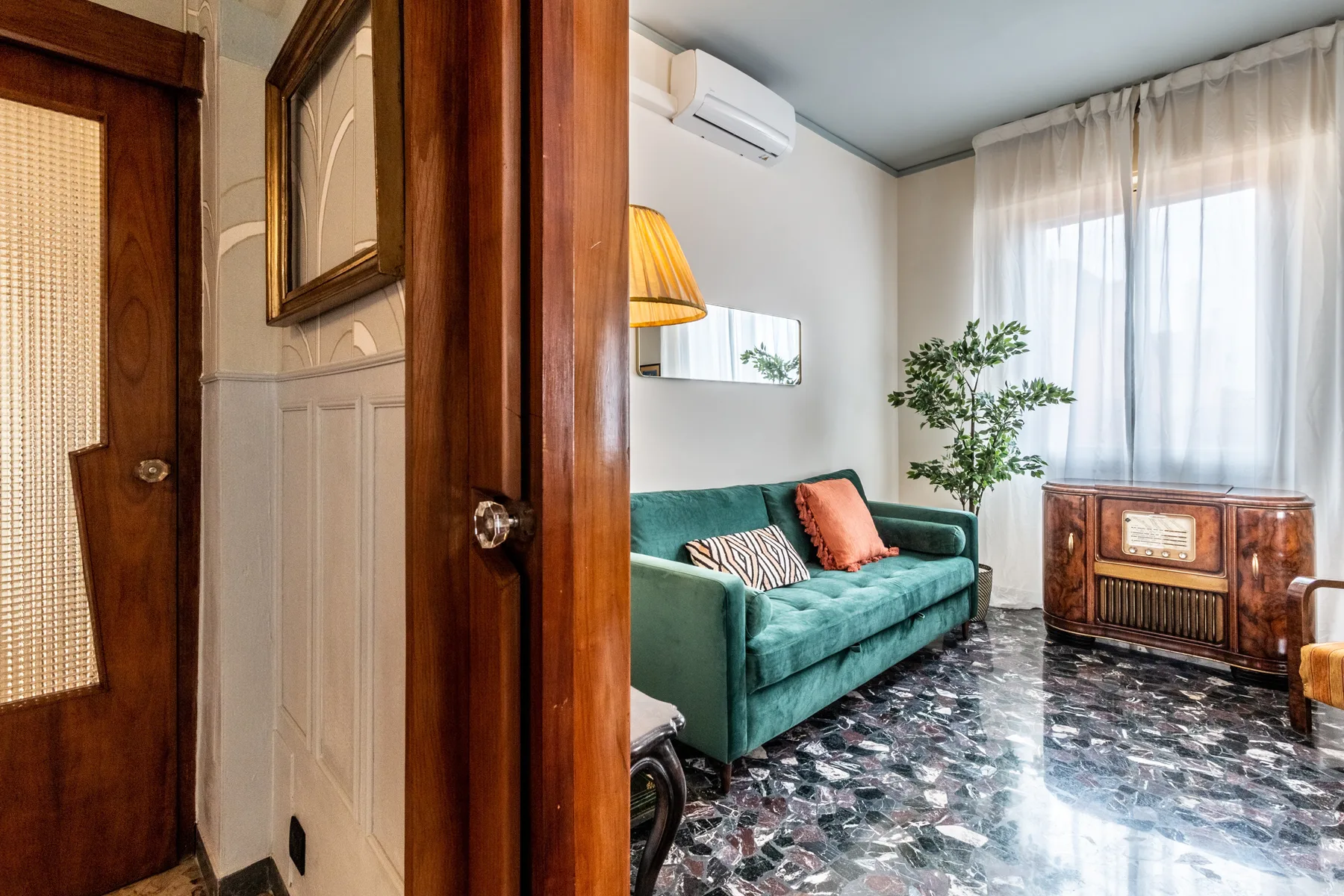 Una sala de estar con un sofá verde azulado, una planta frondosa y una ventana grande.