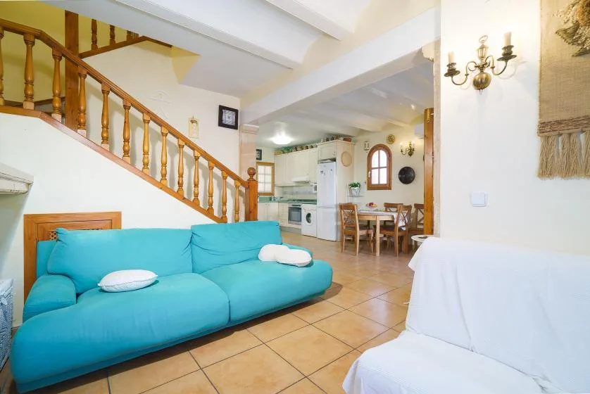 Sala de estar con asientos turquesa bajo una escalera de madera y un comedor al fondo.