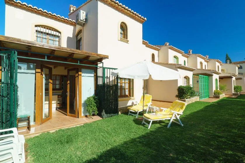 Un patio soleado con asientos al aire libre y sombrillas junto a un edificio blanco.