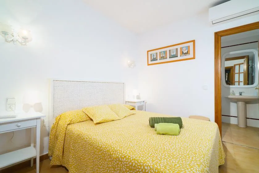 Un dormitorio con una colcha amarilla estampada y una mesita de noche blanca.