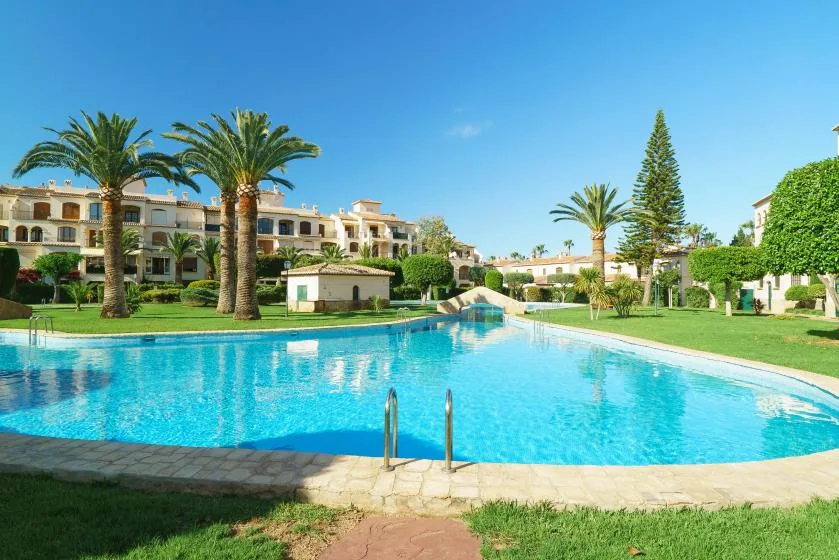 Una gran piscina al aire libre está rodeada de palmeras y jardines.