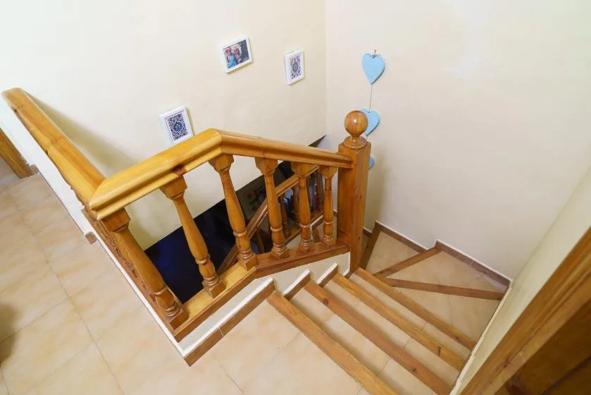Una escalera de baldosas con pasamanos de madera baja junto a una pared color crema.