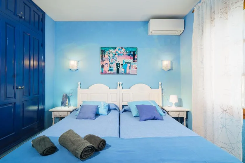 Un dormitorio azul con dos camas, luces de pared y una ventana con cortina.