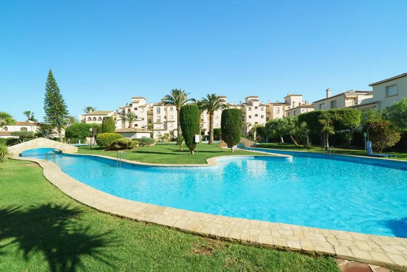 Una piscina exterior curva está rodeada de jardines y edificios de apartamentos.