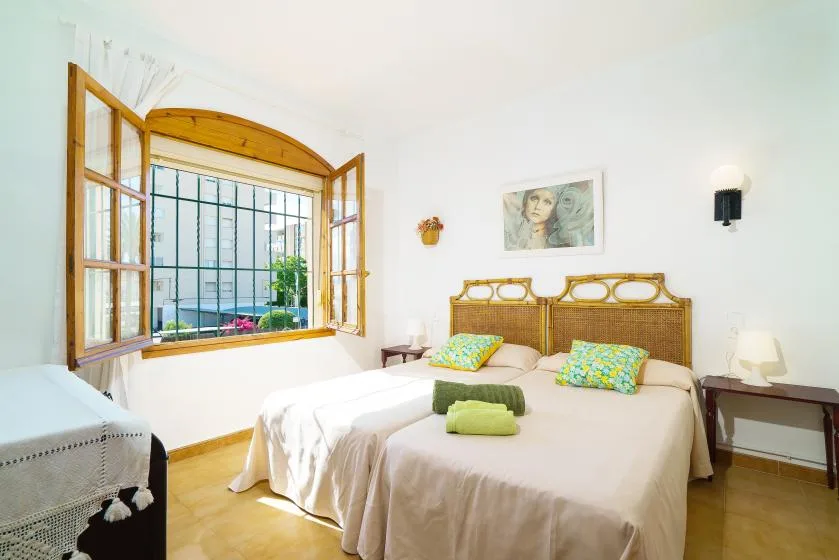 Un dormitorio luminoso con una cama y una ventana abierta con marco de madera.