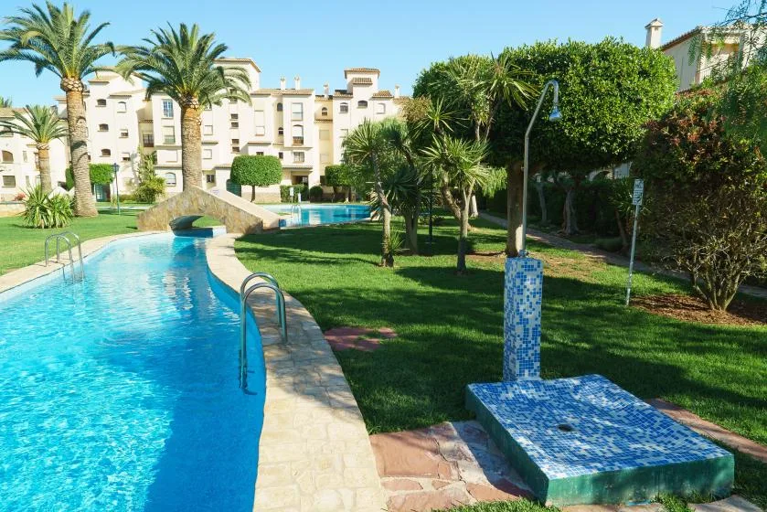 Una piscina al aire libre se curva por un patio ajardinado con palmeras.