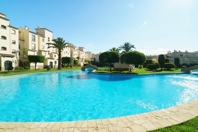 Una gran piscina al aire libre está rodeada de jardines y edificios de apartamentos.