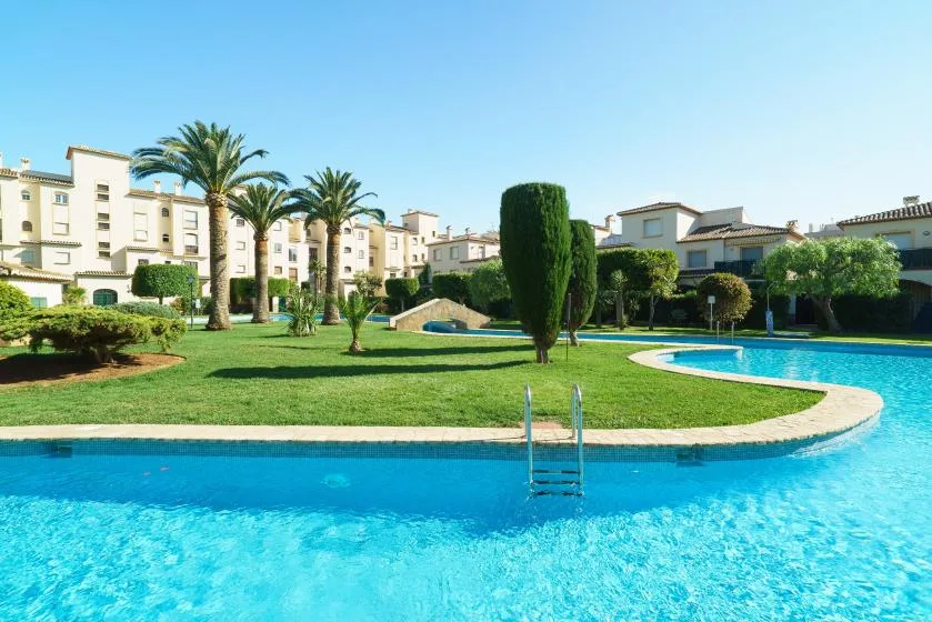 Una piscina exterior rodea un césped verde con palmeras.
