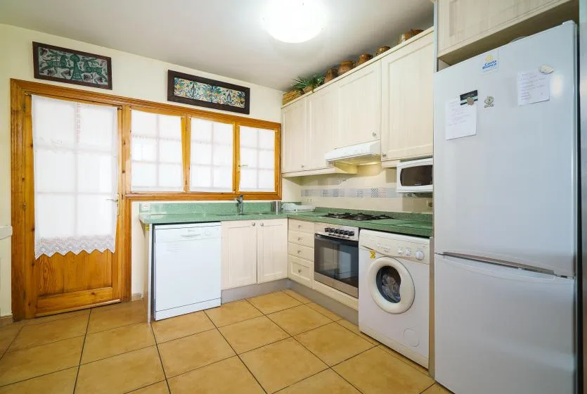 Una cocina luminosa con encimeras verdes, armarios blancos y un refrigerador.