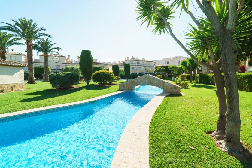 Una piscina curva atraviesa un jardín ajardinado con palmeras.