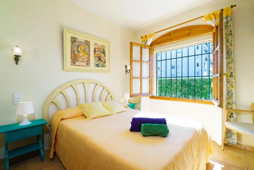 Un dormitorio con una cama bajo una ventana abierta con vistas a la vegetación.