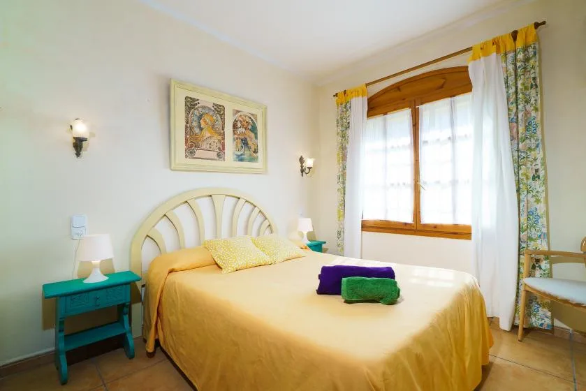 Un dormitorio con una cama bajo cuadros enmarcados y una ventana luminosa con cortinas.