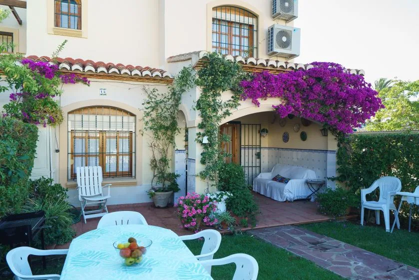 Un patio ajardinado con asientos al aire libre, enredaderas floridas y una cama de día a la sombra.
