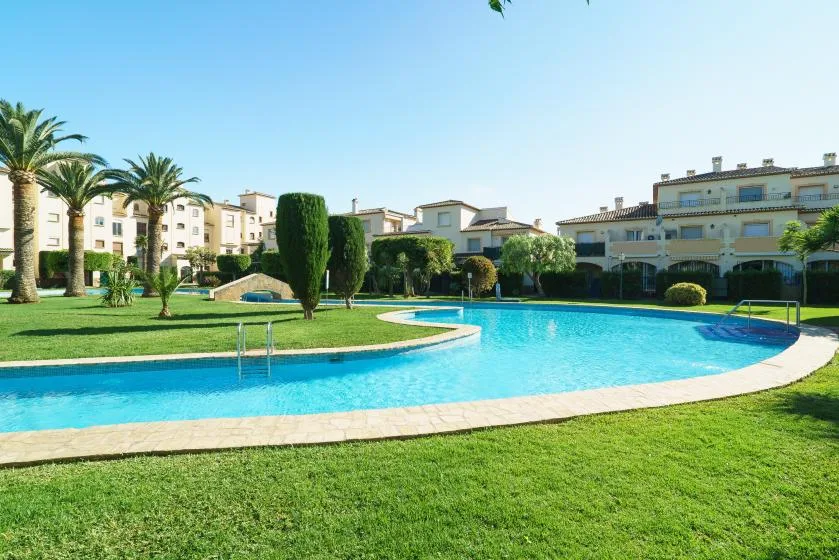 Una piscina exterior curva está rodeada de césped y edificios de apartamentos.