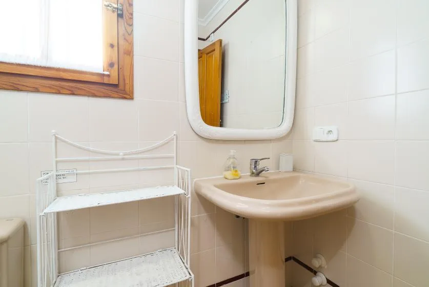 Una esquina de baño alicatado con lavabo, espejo y estantería blanca.