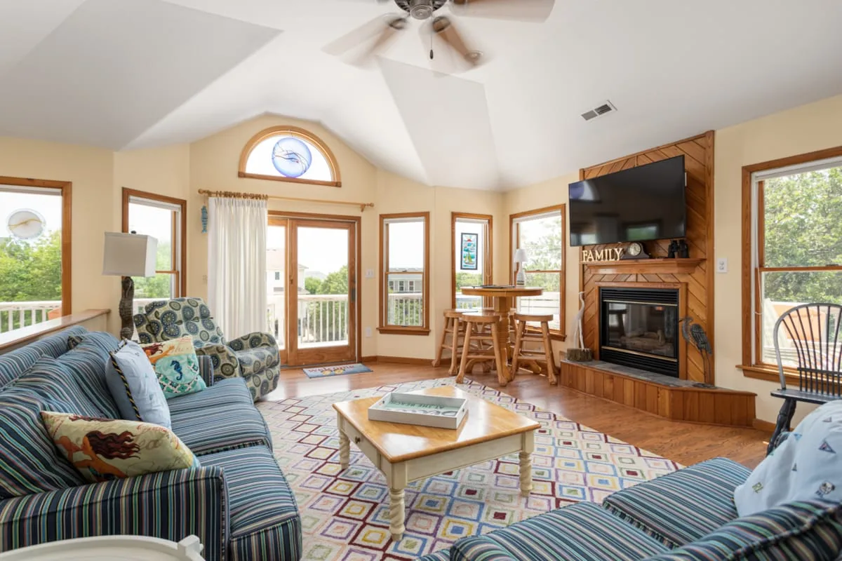 A bright living room with patterned seating and a fireplace beneath a mounted television.
