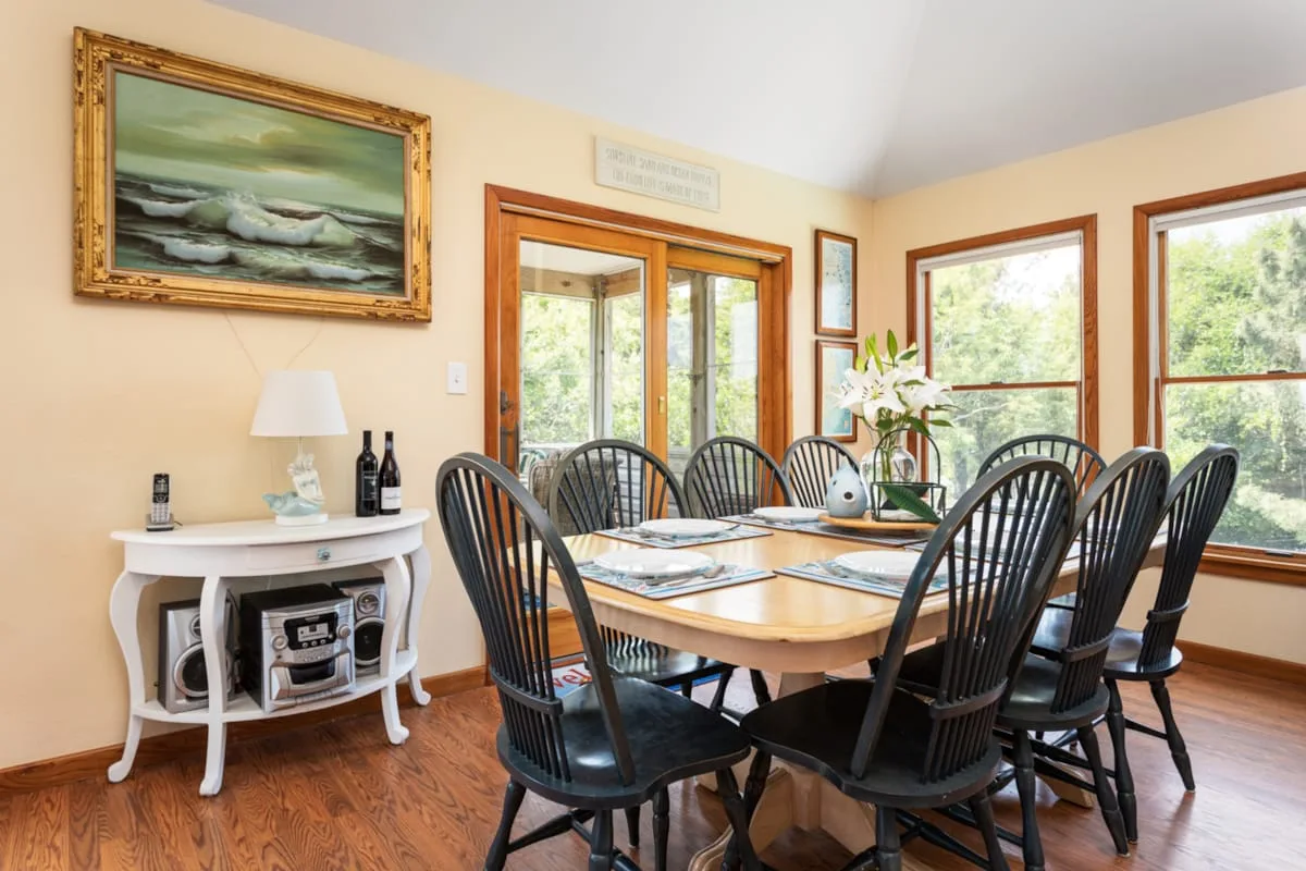 A dining room with a long table and chairs beside large windows.