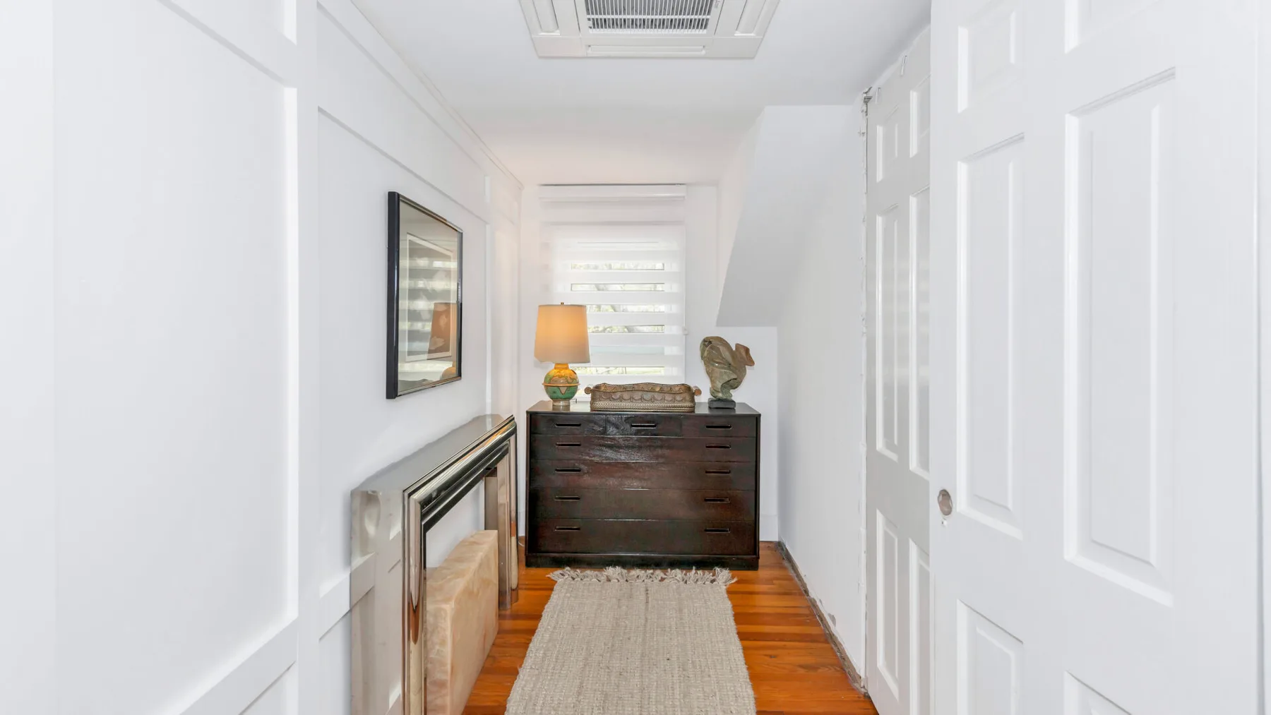 A bright hallway with a dark wooden dresser and a rug.