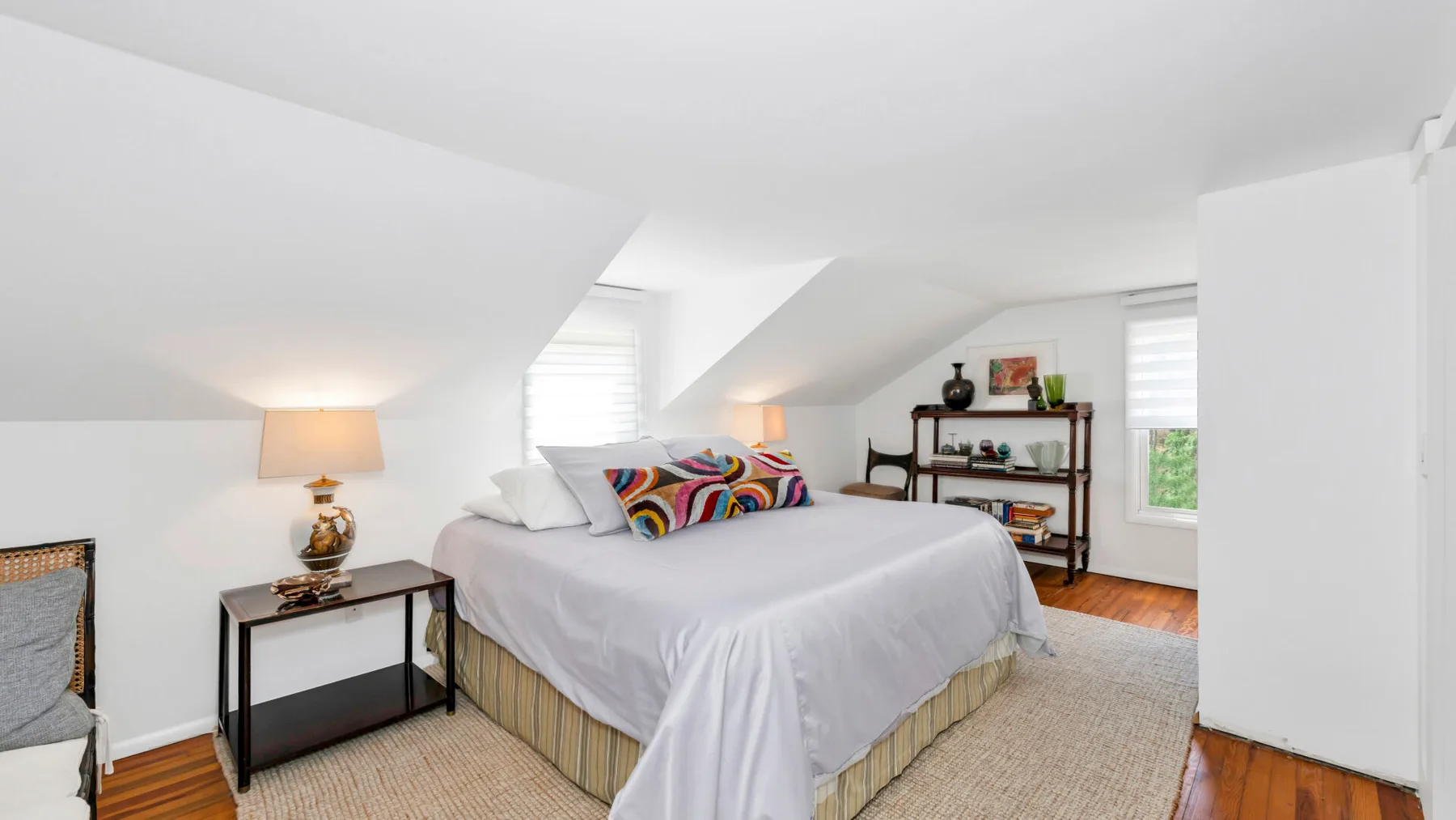 A bedroom with a bed, bedside table, and shelving beneath a sloped ceiling.