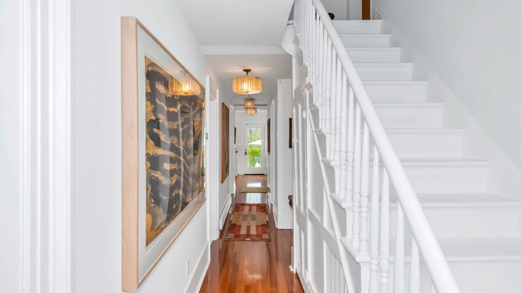 A bright hallway with framed artwork and a staircase.