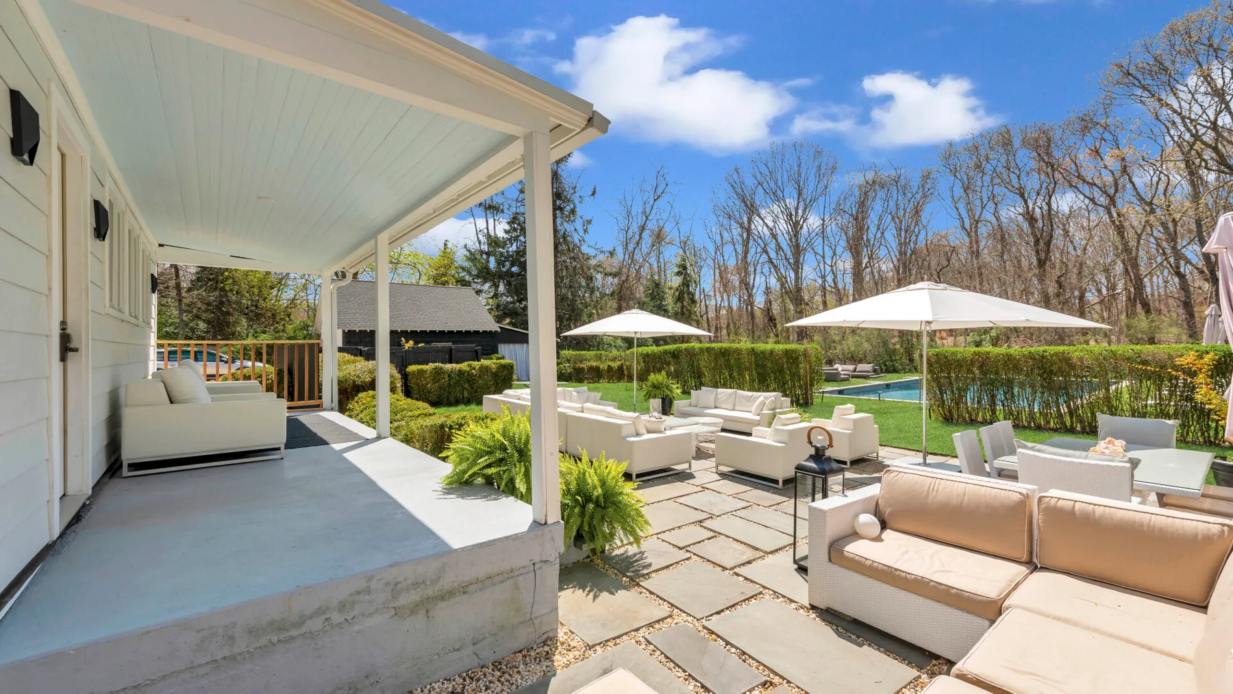 A covered patio opens onto an outdoor seating area beside a swimming pool.
