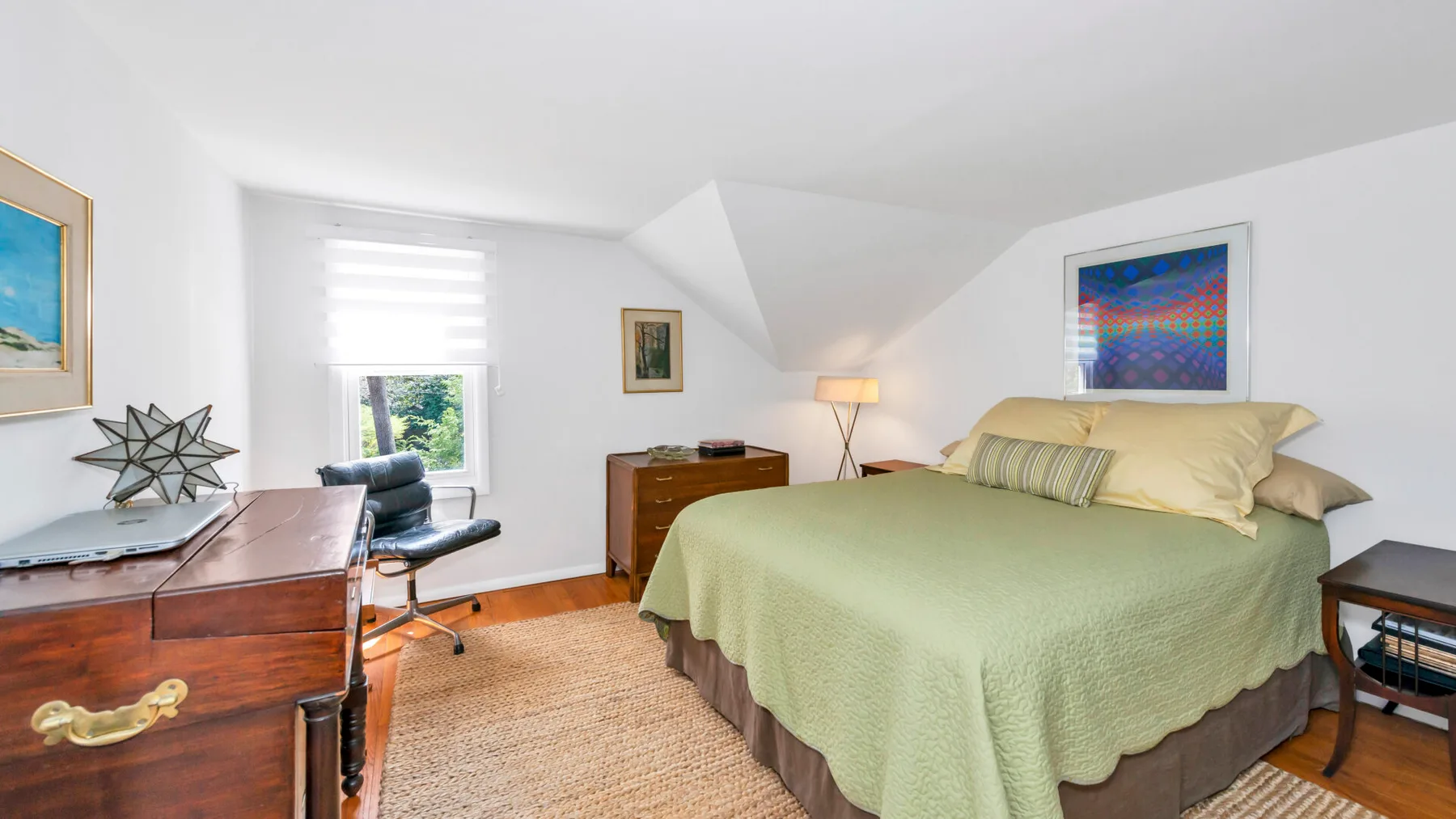 A bright bedroom with a large bed, a desk, and a window.