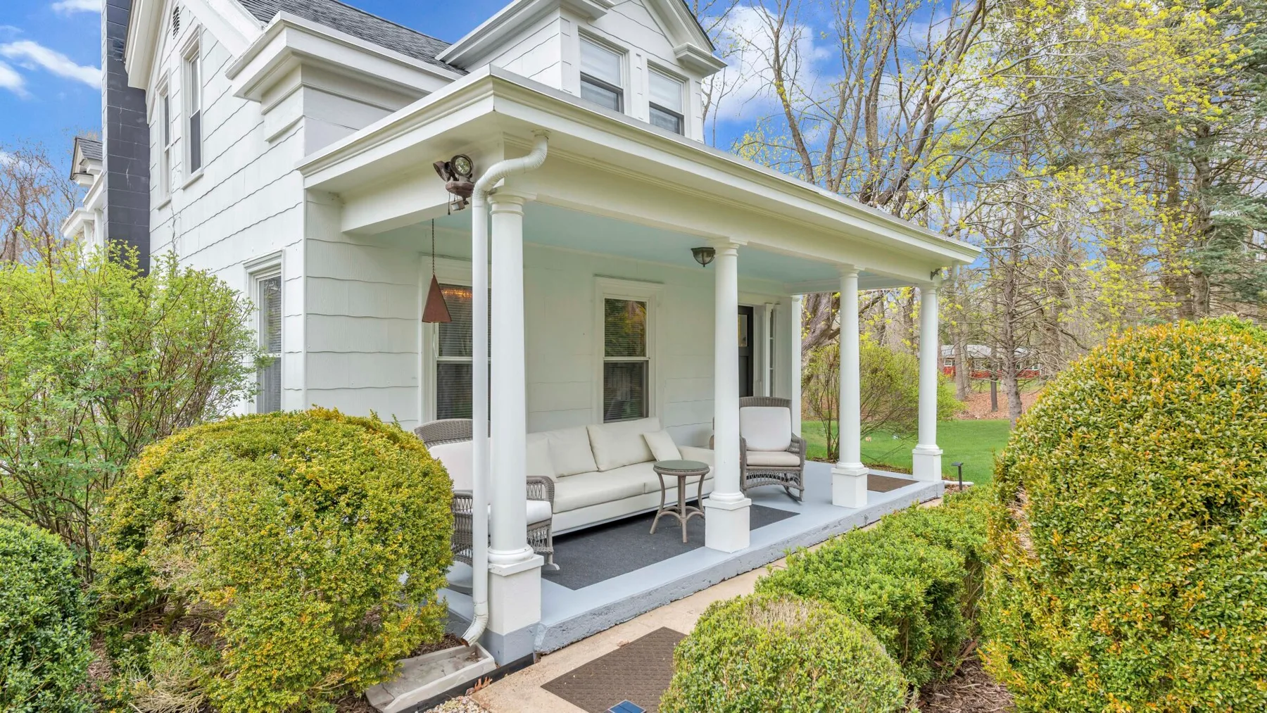 A white house with a covered front porch and surrounding shrubs.