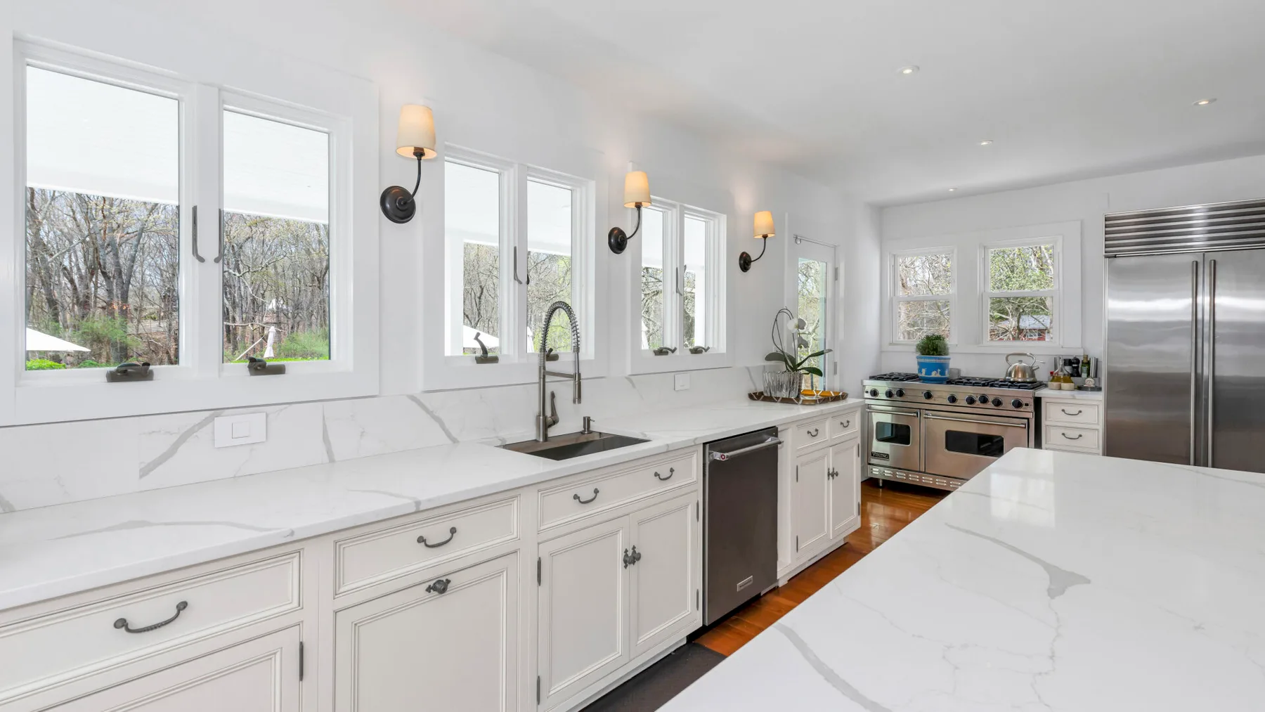 A bright kitchen with white cabinetry, a long counter, and stainless steel appliances.