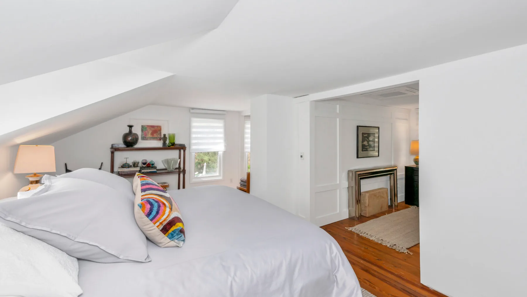 A bedroom beneath a sloped ceiling, with a bed and an adjoining sitting area.